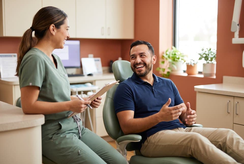 A man laughing with a dental hygienist as he sits in the dental chair before a routine cleaning
