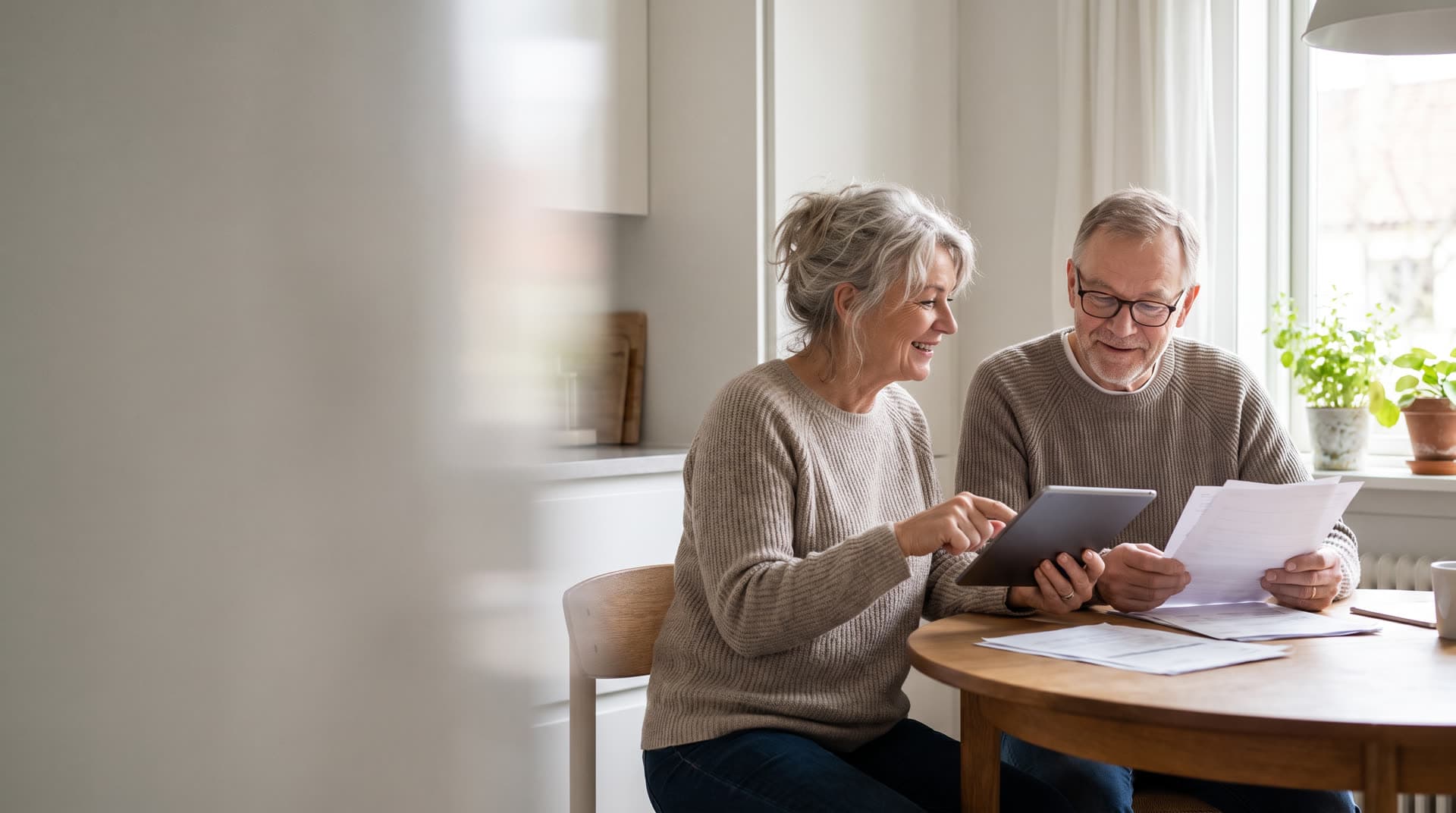Couple in their sixties reviewing papers and a tablet together at a kitchen table