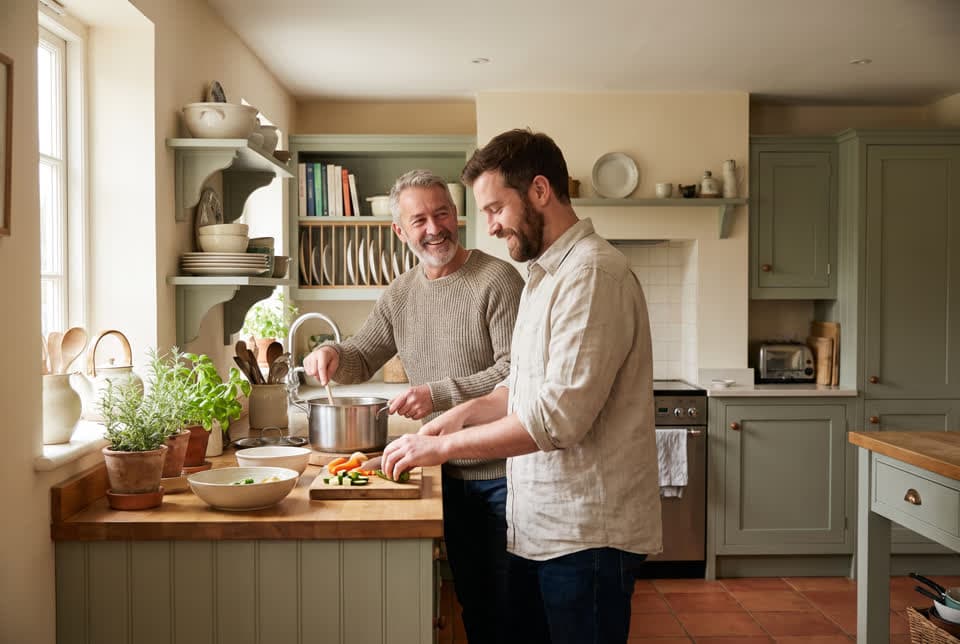 An older man and his adult son cooking a meal together in a warm home kitchen