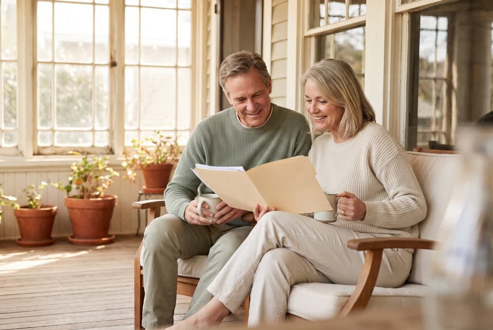 A couple on a sunny porch with mugs of coffee, looking through a folder of papers together