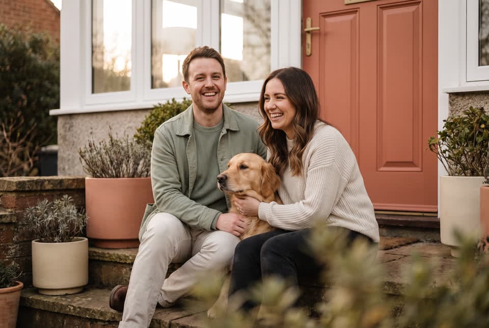 A smiling couple sitting on the front steps of their house with their golden retriever
